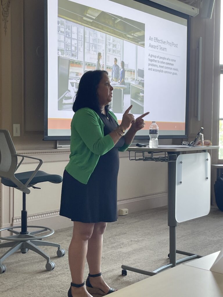 Kris Monahan presents to research administration professionals during a RIRAC workshop at Salve Regina University. Participants are seated throughout the room, viewing a projected presentation focused on strengthening collaboration across research administration services.